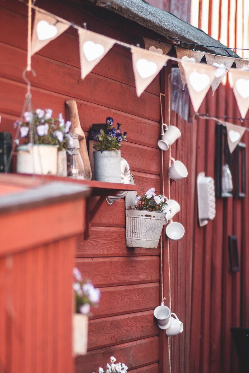 Uteserveringen vid den röda väggen med vimplar, hyllor och blommor
